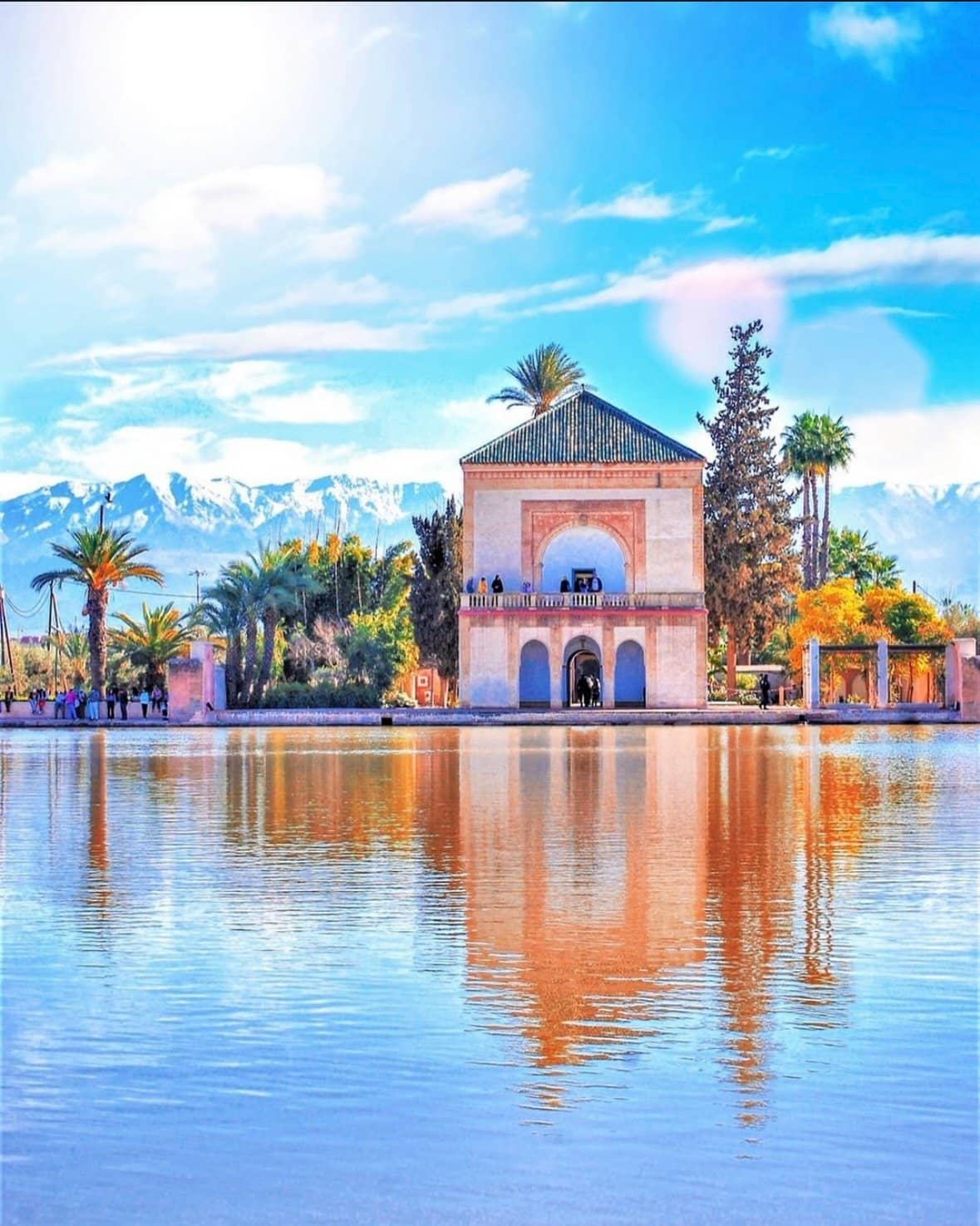 The historic Menara Gardens in Marrakech, Morocco, featuring a large reflective basin, a traditional pavilion, and the Atlas Mountains in the background