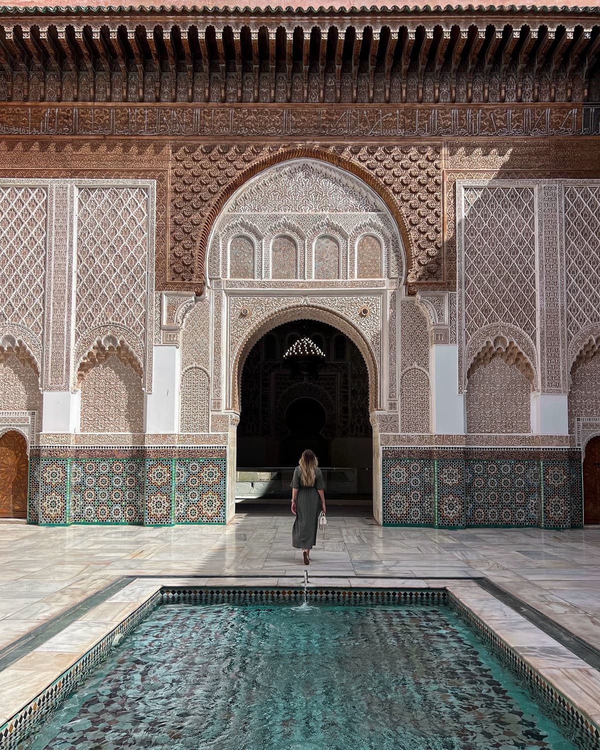 Solo female traveler admiring the historic architecture of Ben Youssef Madrasa, one of the most famous attractions in Marrakech, Morocco