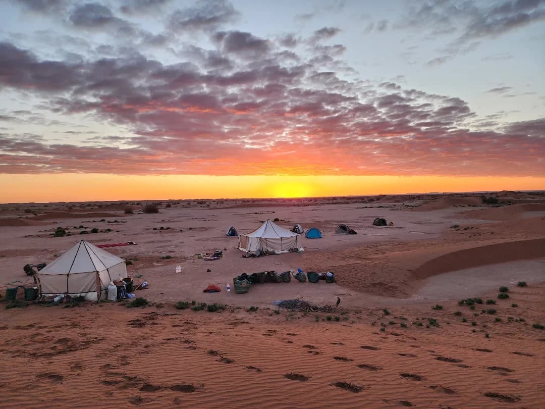 Camping in Morocco with traditional desert tents in the Sahara under a colorful sunset sky