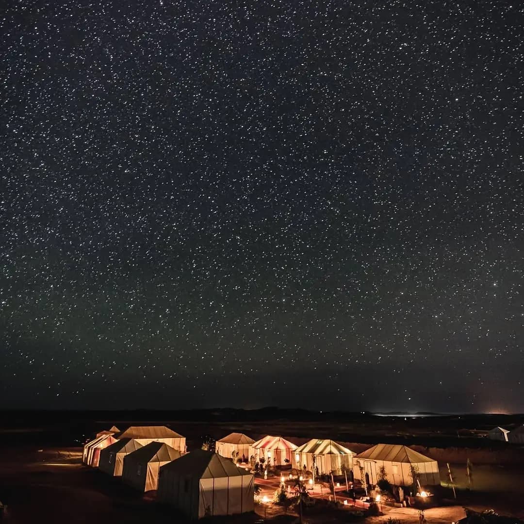 Sahara at Night in Merzouga, Morocco, with desert dunes and an overnight camp beneath a star-filled sky