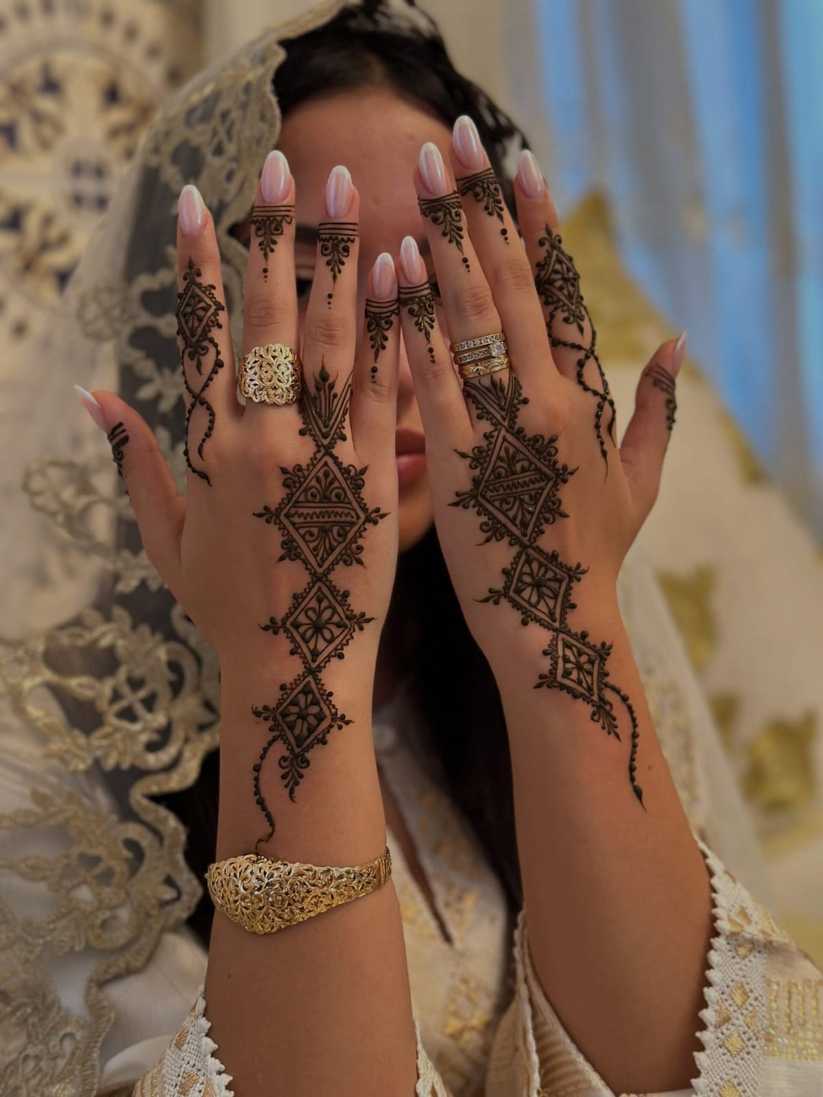 Moroccan bride displaying traditional henna designs on her hands during a wedding celebration, wearing gold jewelry and embroidered bridal attire